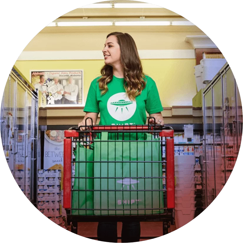 A woman in a green Shipt t-shirt pushing a shopping cart.