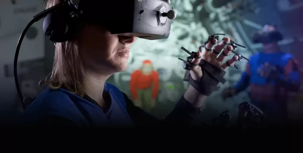 A woman in VR goggles wearing an advanced hand-tracking glove with her hand in the raised.