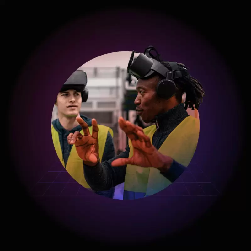 A man in VR goggles and a yellow vest explaining how to use the equipment to another man in VR goggles and a yellow vest.