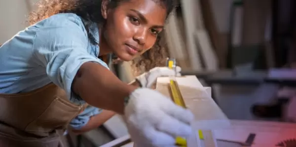 A woman measuring a board with a tape measure.
